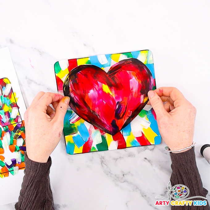 Image featuring a hand glueing the large heart to its background to complete the pop art heart painting.