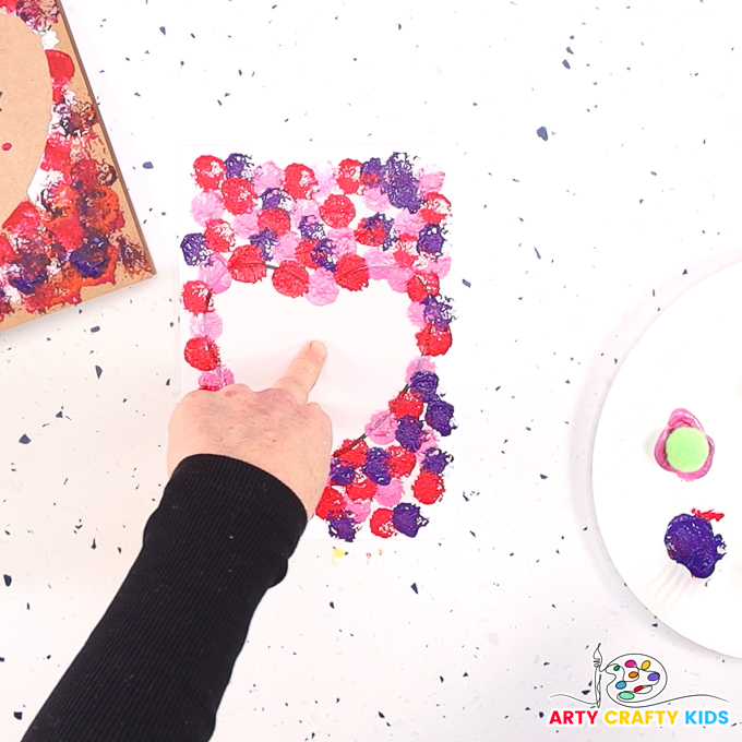 Image of a hand holding the heart template onto a painted Valentine Day card.