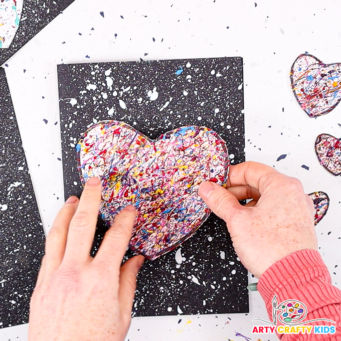 Image of a hand glueing the heart onto the black card with white splats.