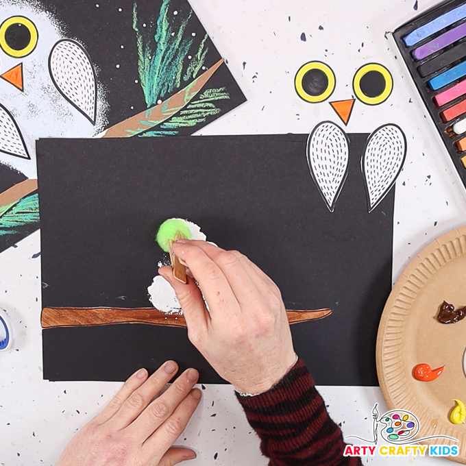 Image featuring a hand using a sponge attached to a clothes peg to paint the owl.