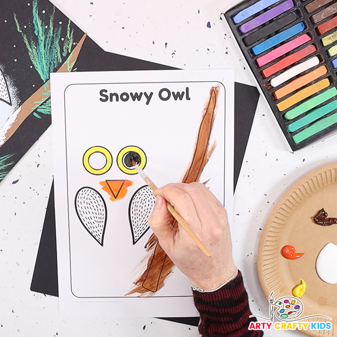 Image featuring a hand painting the owl's eyes, beak and the branch.