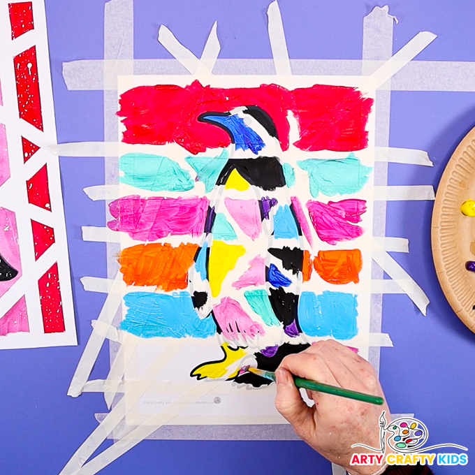 Image of a hand painting the penguin over, brushing over the tape.