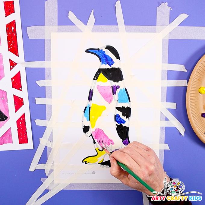 Image of a hand painting the penguin over, brushing over the tape.