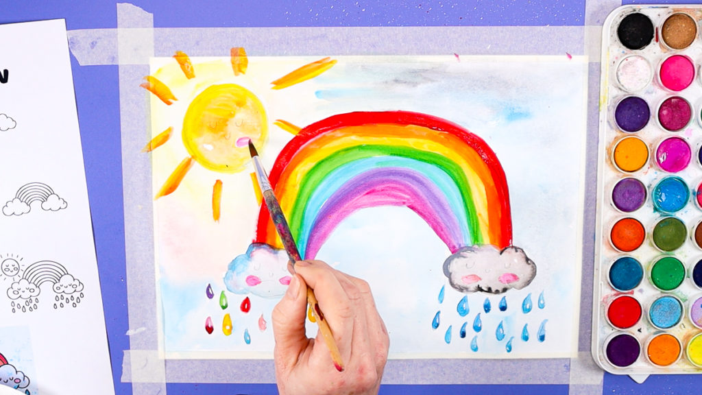 Image of a hand painting cute cheeks on the sun and clouds.