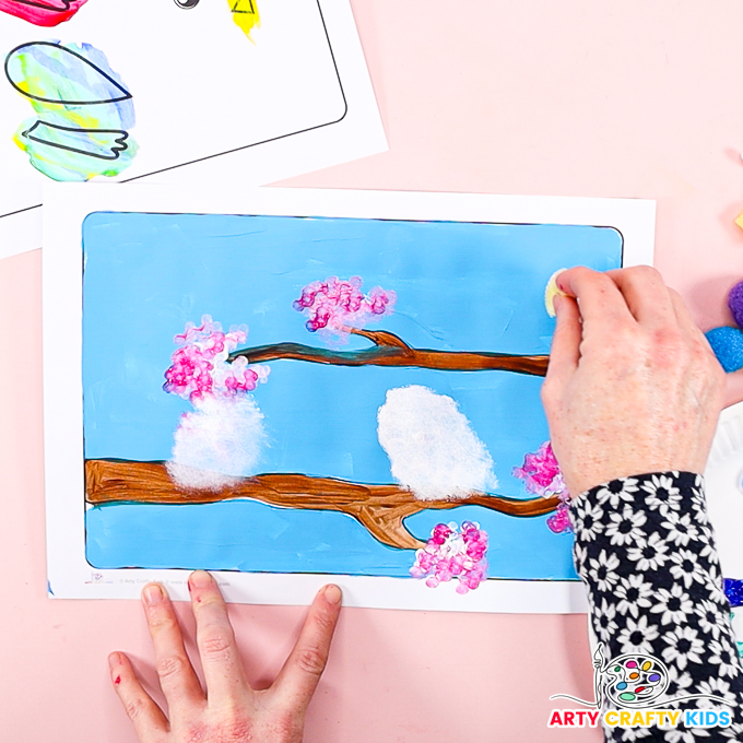 Image of a hand sponge painting white ovals onto tree branches.