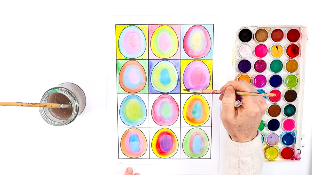 Image of a hand painting the surrounding squares in a contrasting color to the contained egg.