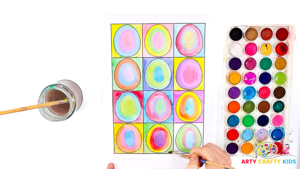 Image of a hand completing the Kandinsky Watercolor Easter Egg art project. The eggs are painted in lots of different color combinations to mimic the style of concentric circles.