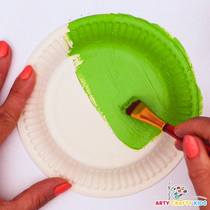 Image of a hand painting a paper plate green - this is the body of the frog.