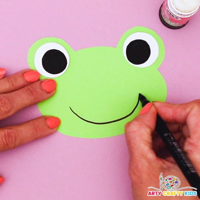 Image of a hand drawing a big smile onto the head of the frog.