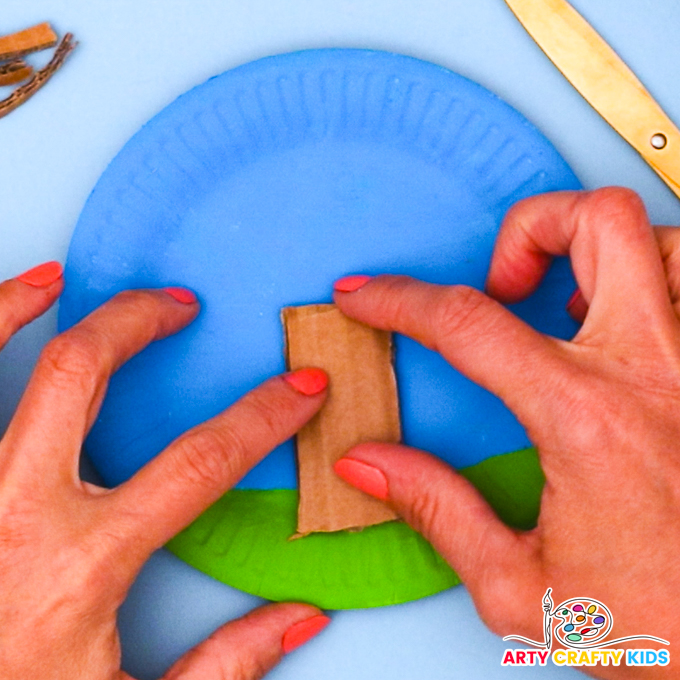 Image of a hand glueing the trunk of the Spring tree to the grassy area of the paper plate.