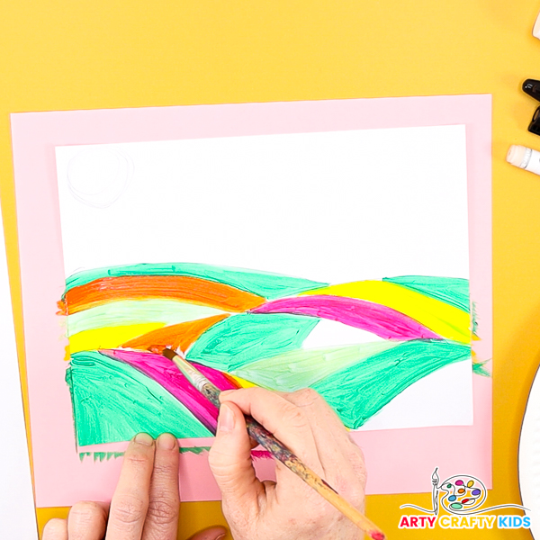 Image of a hand painting some of the hills orange, pink, yellow and red.