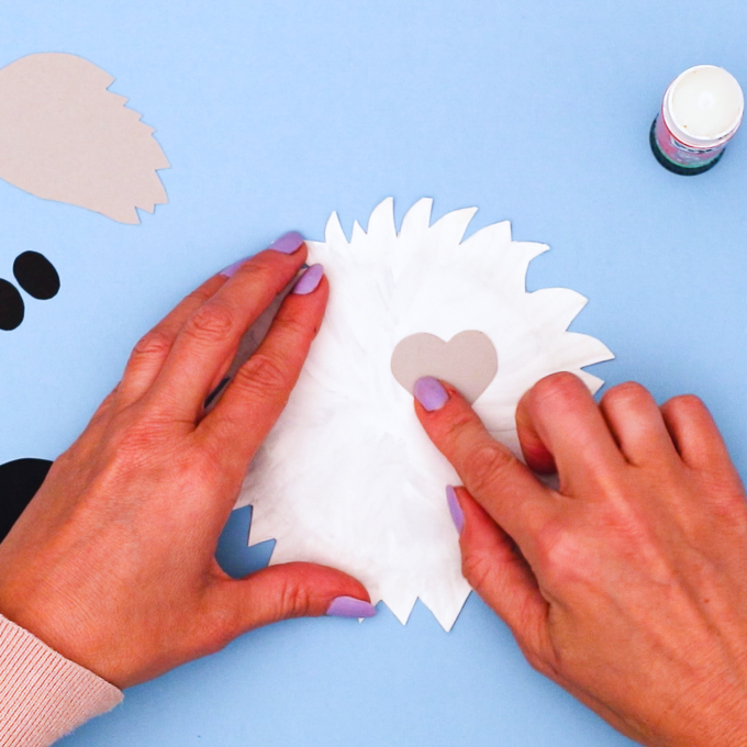 Image of a hand glueing a heart eye patch onto the paper plate.