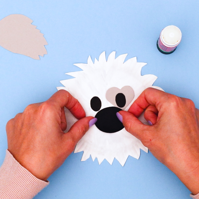 Image of a hand glueing the dog's nose and eyes onto the paper plate.
