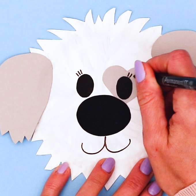 Image of a hand using a black marker pen to draw eyelashes and a smile onto the paper plate.