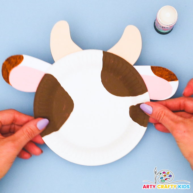A hand holding up the paper plate to showcase the newly affixed ears and horns.
