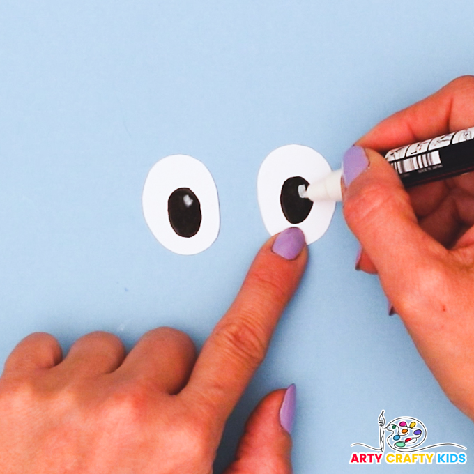 A hand finishing off a pair of eyes by drawing white dots into the pupils.