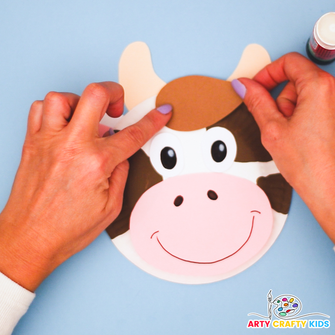 A hand affixing the brown hair piece between the cow's horns.