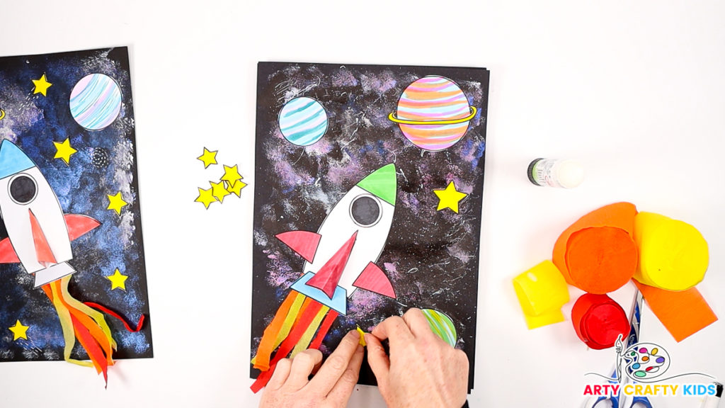 Image of a hand gluing the planets and stars around the spaceship.