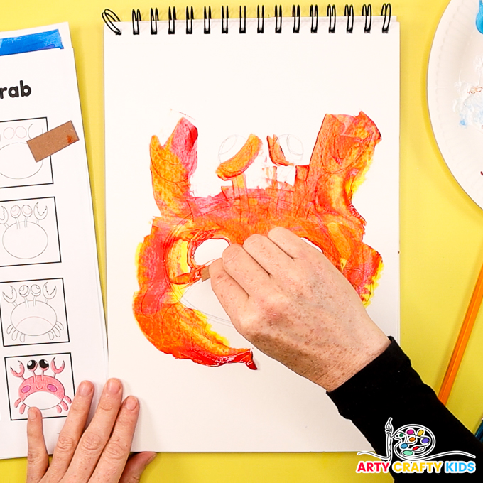 Image shows a hand scraping the paint across the crab, leaving the stomach, cheeks and eyes white.