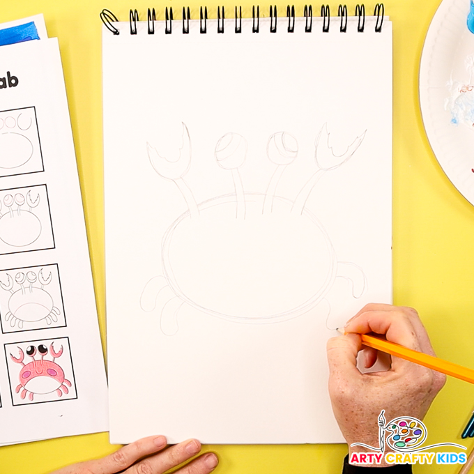 The image shows a hand using a pencil to draw the legs of the crab.