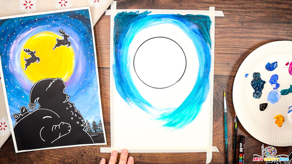 A step-by-step Christmas craft featuring a painted night sky in progress, with shades of blue swirling around a blank circular moon template. The completed Santa silhouette artwork is shown on the left as inspiration, while paints, brushes, and a palette with various colors are displayed on the right, ready for use.