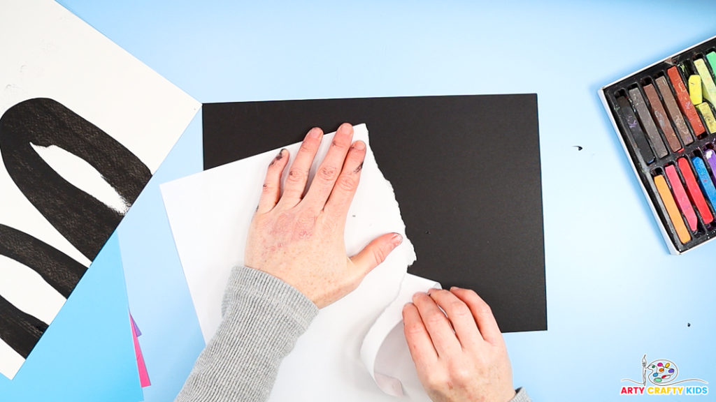 Image of a hand tearing white paper to create a jagged edge in preparation for creating the Southern lights with chalk pastels.