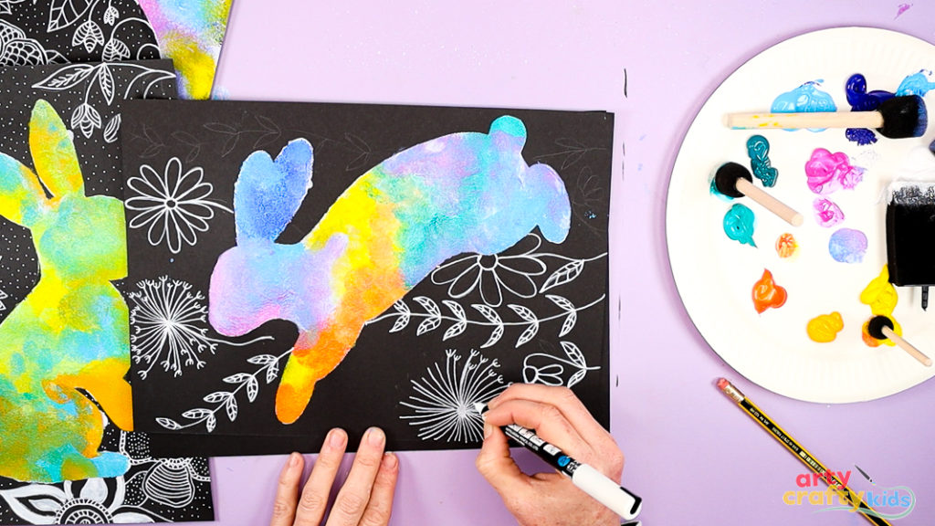Image of a hand drawing flowers and leaves around the bunny silhouette painting.