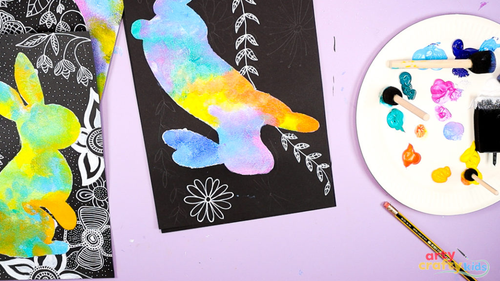 Image of a hand drawing flowers and leaves around the bunny silhouette painting.