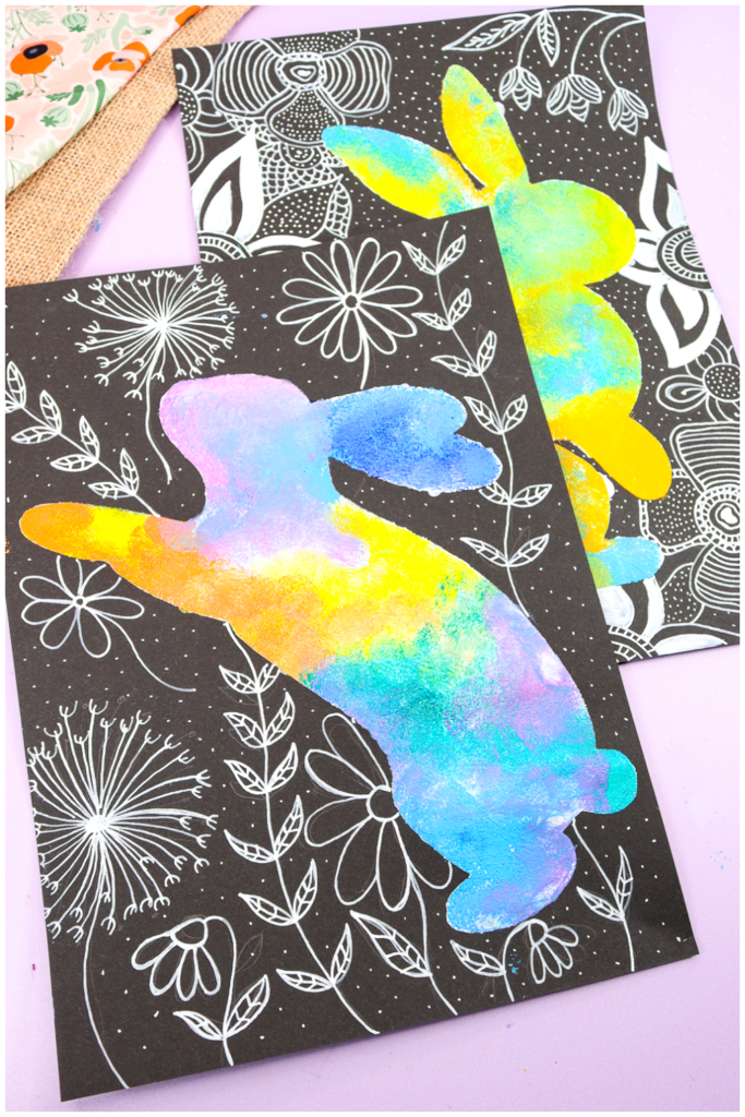 Colourful sponge-painted bunny silhouette on black paper, surrounded by intricate white doodle flowers and patterns. A creative Spring or Easter art project for kids exploring colour blending and contrast.