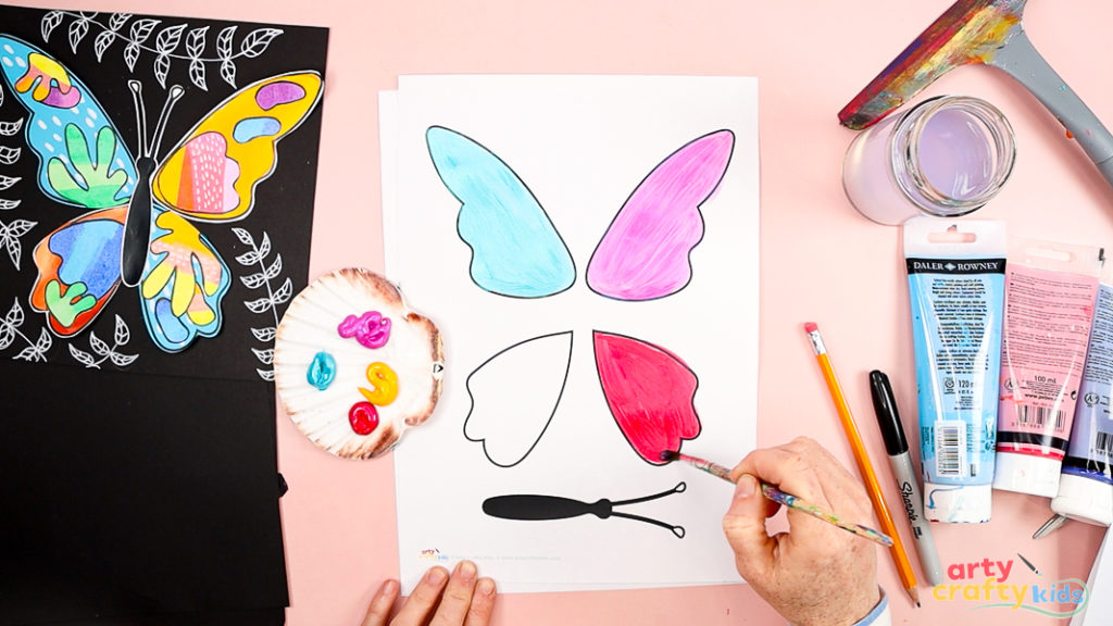 Image featuring a hand painting the butterfly wings in block colors of blue, pink and red.