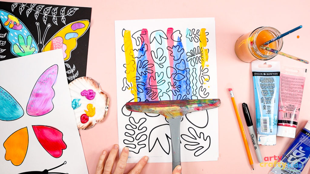 Image of a hand using a squeegee to scrape the paint across the Matisse inspired template.