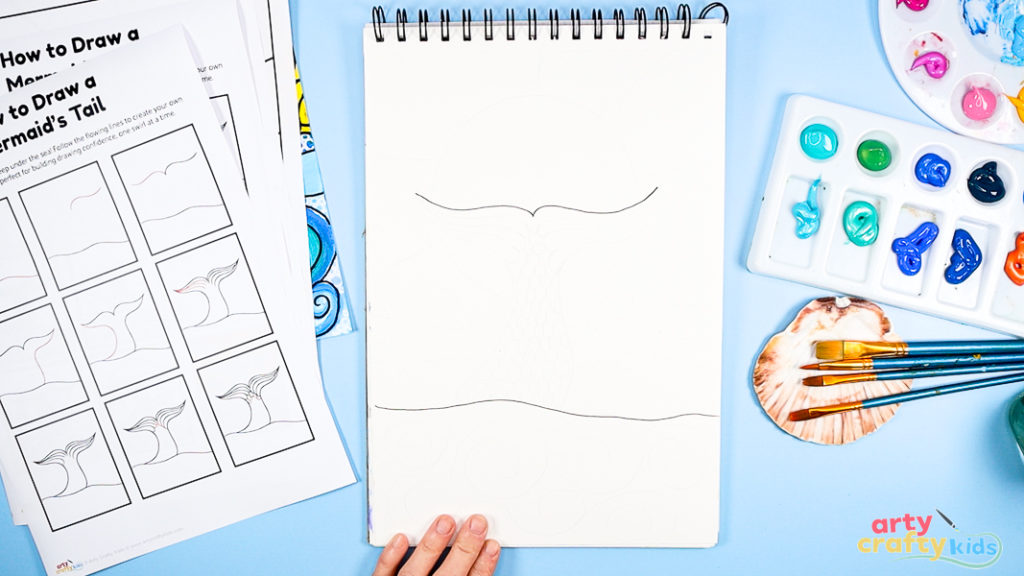 Image of Step 1: Drawing the first curved lines to form the base and flukes of the mermaid’s tail, using light pencil strokes on white paper.