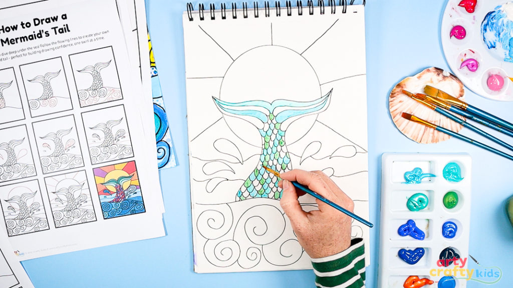 Image of Step 6: Painting the mermaid tail with acrylic paint in cool or warm colors, showing blending techniques and layered brushstrokes.