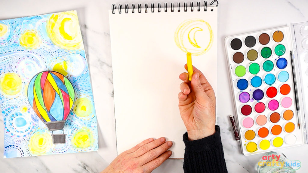 Image featuring a hand holding up a yellow oil pastel with a crescent moon drawn in the background.