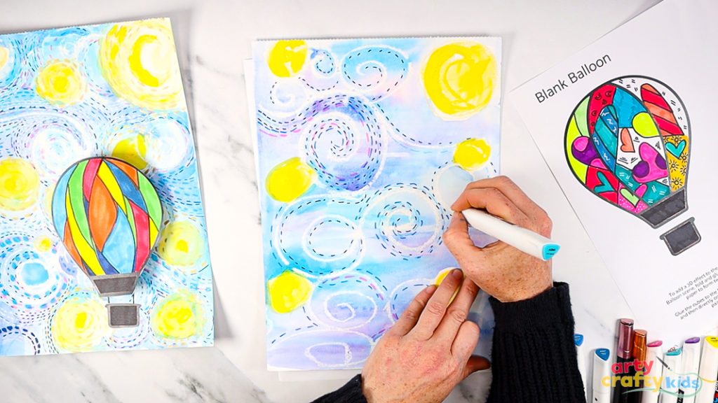 Image of a hand using a blue marker pen to draw a collection of dashed lines around the white wax swirls - adding movement to the Starry Night sky.