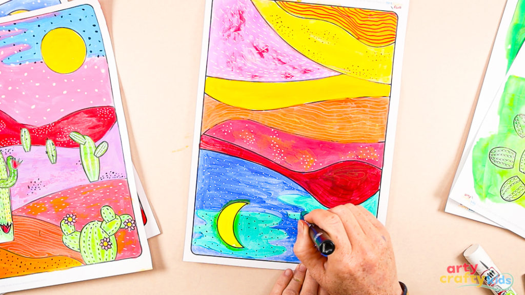 Image of a hand drawing white and black dots within the sky area of the desert scene.