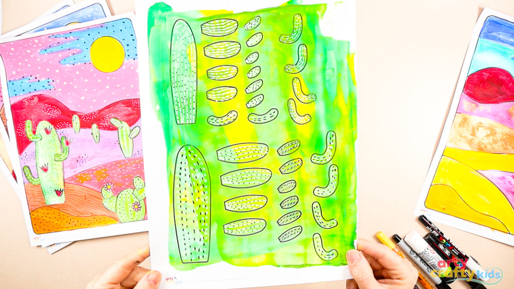 Using a black marker to add doodle patterns to painted cactus template pieces on a green and yellow background.