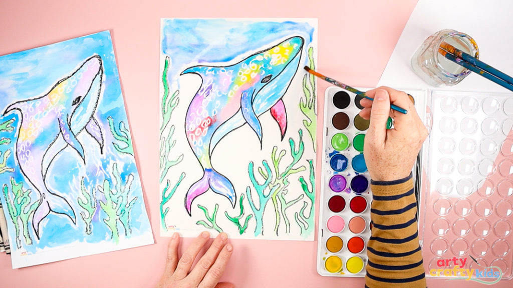 Image of a hand using the wet-on-wet technique to paint the ocean blue and the seaweed various shades of green.
