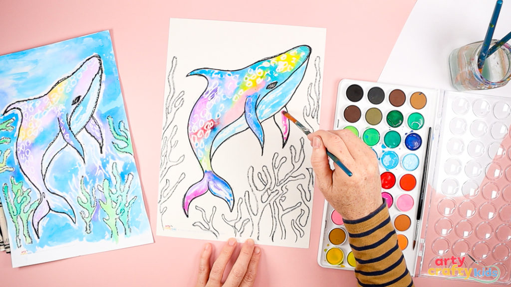 Image of a hand painting the whale shark's upper body with watercolor paint ( mixture of blue, red, pink, and purple).