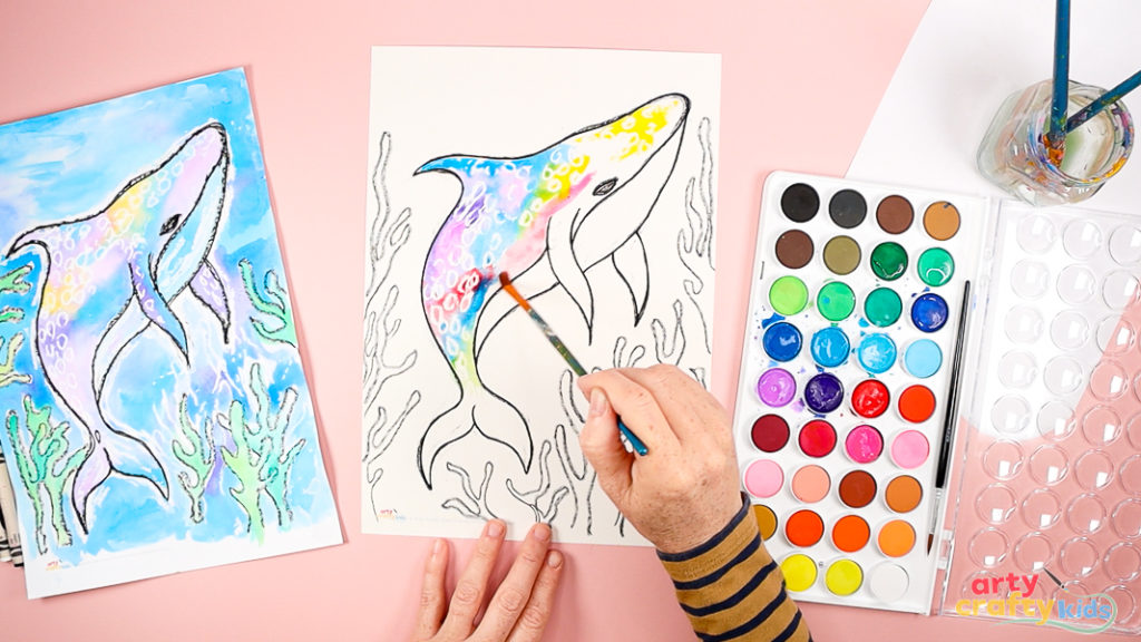 Image of a hand painting the whale shark's upper body with watercolor paint ( mixture of blue, red, pink, and purple).