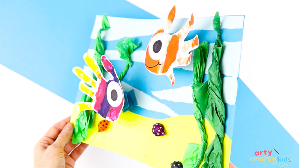 Close-up of a handprint fish glued onto accordion-fold paper springs, creating a 3D swimming effect.
