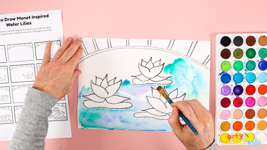 Image of a hand painting the space around the water lilies, a mix of blue, lilac and green.