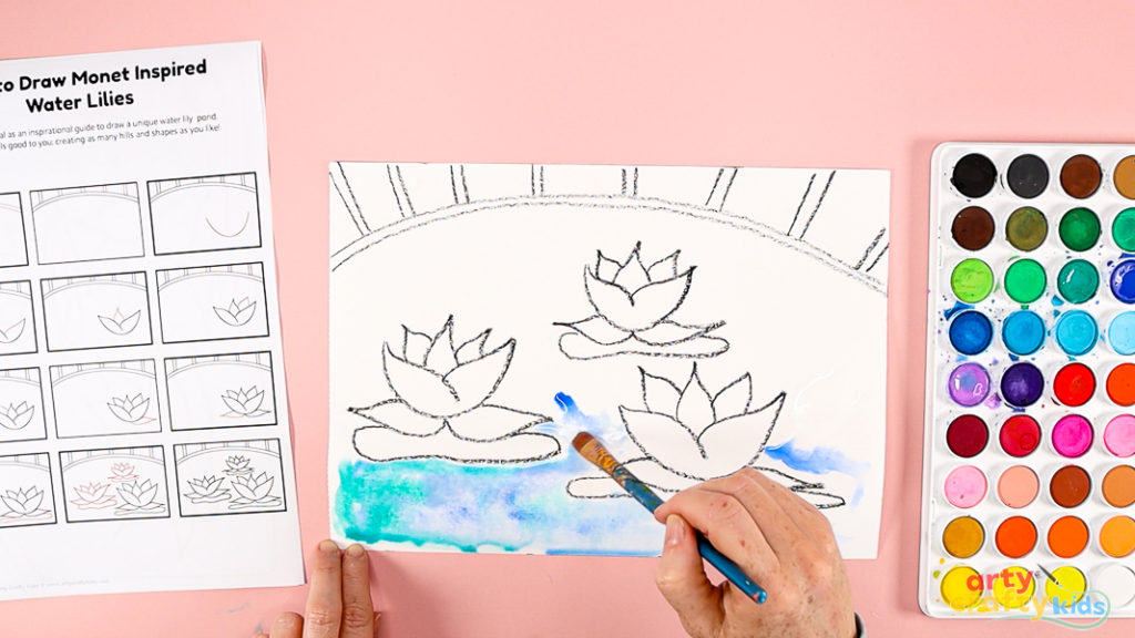 Image of a hand painting the space around the water lilies, a mix of blue and green.