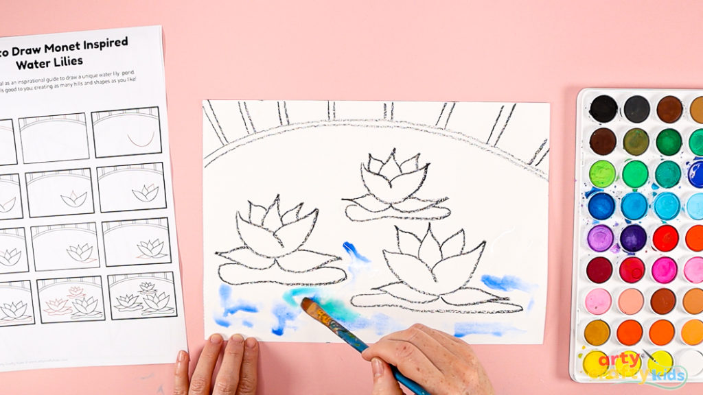 Image of a hand painting the space around the water lilies, a mix of blue and green.