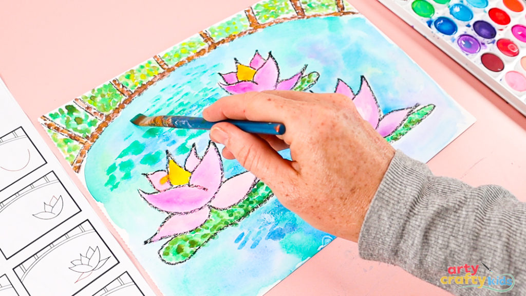 Image of a hand layering green paint with a flat-tipped brush over the watercolor pond.