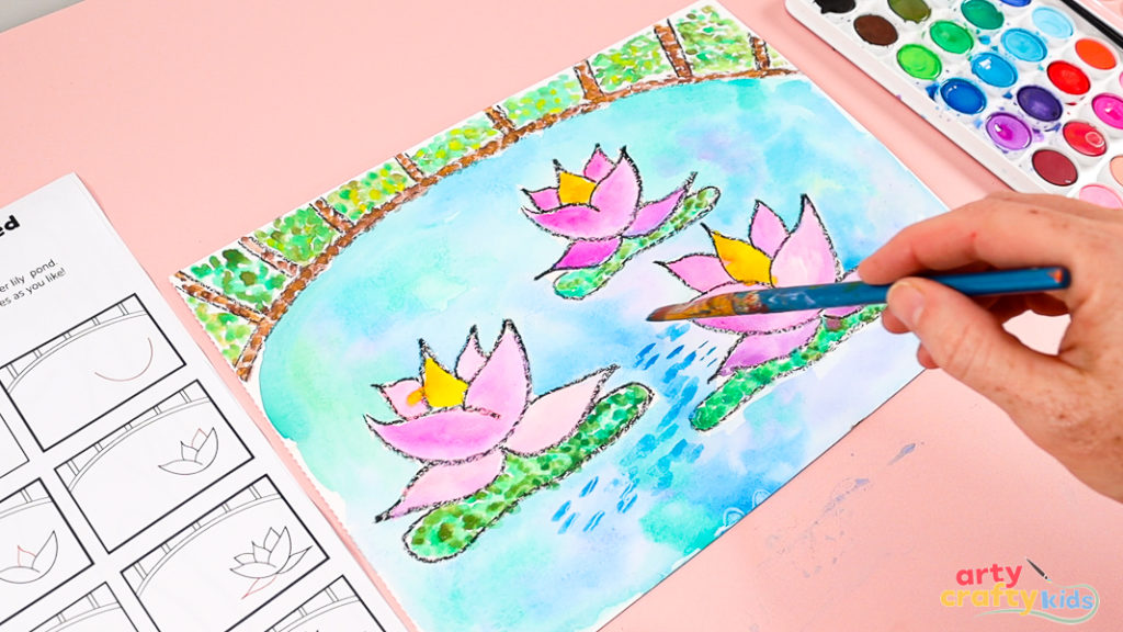 Image of a hand layering blue paint with a flat-tipped brush over the watercolor pond.