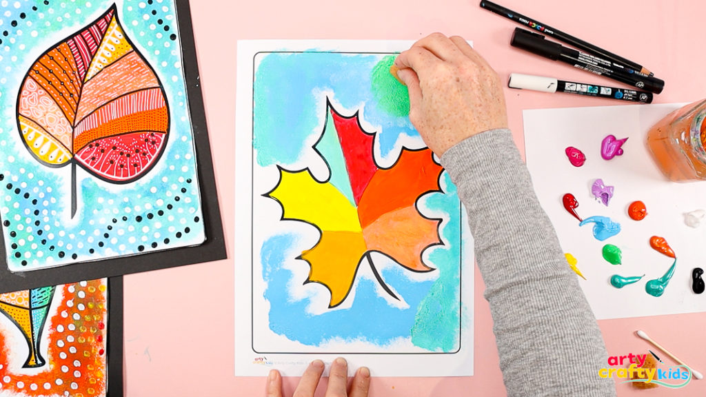 Image of a hand using a sponge to paint the background in a contrasting blue color. 