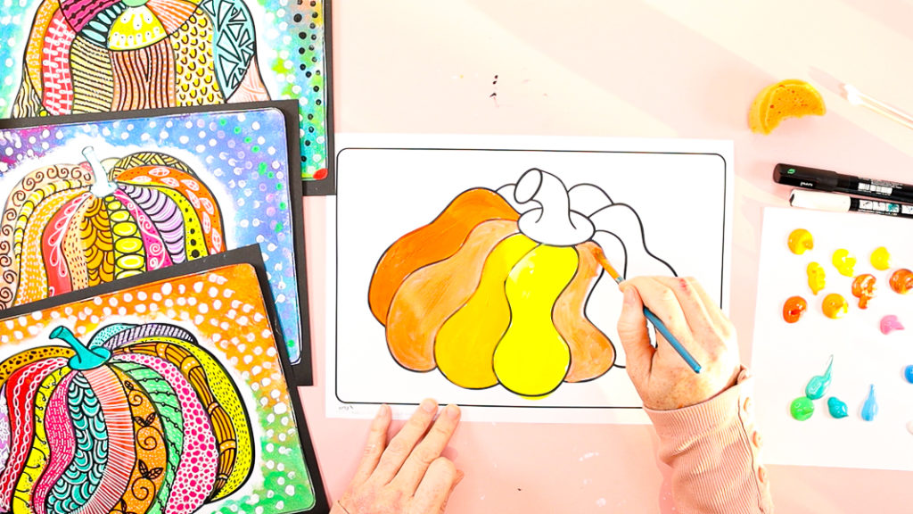 Image of a hand painting the pumpkin in yellows and oranges. 