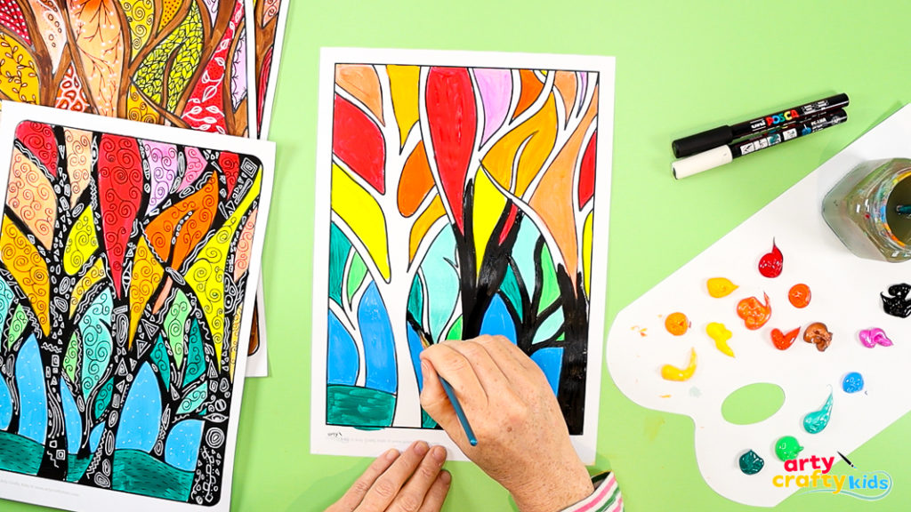Fall tree art in progress with colorful foliage painted and black trunks being added with a brush.