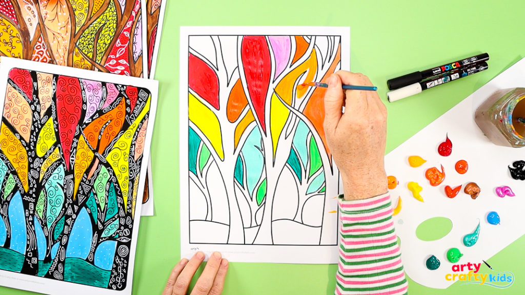 painting foliage sections of a fall tree art template with bright paints, surrounded by finished examples.